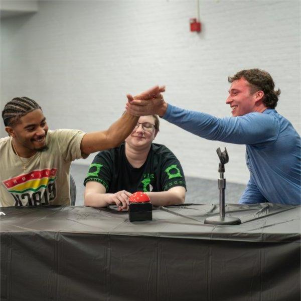 students share a high five while seated at a long table, one student smiles in the middle