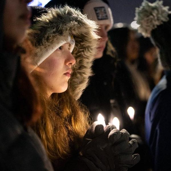 A college student wearing a warm coat is illuminated by candlelight during a vigil.